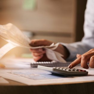 closeup-economist-using-calculator-while-going-through-bills-taxes-office-min-2048x1365